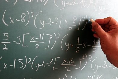 hand writing a maths equation in chalk on a blackboard