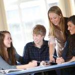 Tutor helping 3 students at desk with studies