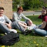 1 girl 2 boys sitting on grass by wall