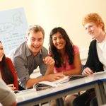 Group of students and tutor sitting at desks laughing together