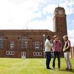Students standing on lawn chatting in front of college building with clock tower