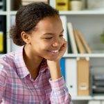 Female student studying on laptop with shelves in the background