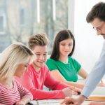 Male tutor explaining studies to group of students at their desks