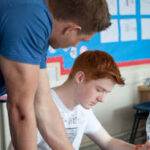 Tutor giving one to one support to student at desk during revision course